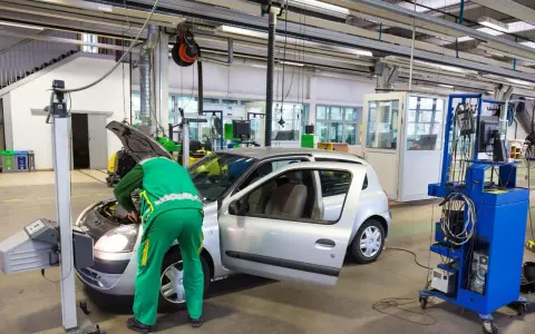 Un meccanico in tuta verde controlla un'auto argentata in un'officina, forse per un controllo secondo l'articolo 80 del codice della strada.