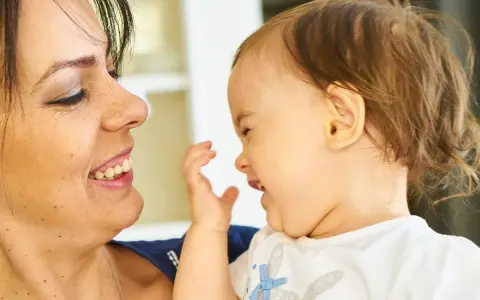Uśmiechnięta mama patrzy na swoje dziecko, które bawi się i śmieje, wyciągając rączkę.