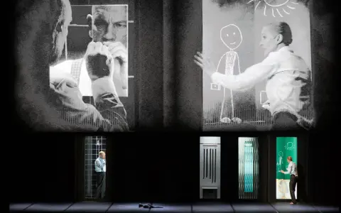 Scena teatralna z projekcjami. Na górze czarno-białe obrazy mężczyzn i kobiety rysującej słońce. Na dole, w oknach, samotność pól bawełnianych, mężczyzna w klatce, przedmioty i kobieta rysująca.