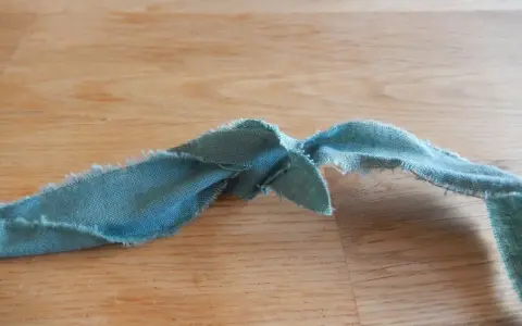 En bit tygremsa, redo att sy ihop trasmattor. Trådar hänger löst från kanterna.
