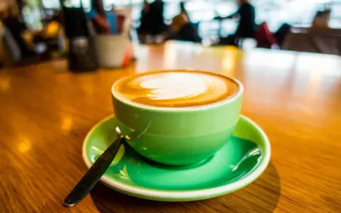 Ein cremiger Cappuccino mit doppeltem Espresso, kunstvoll verziert, in einer leuchtend grünen Tasse auf einem Holztisch.