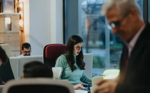 Kobieta w okularach skupiona na pracy przy biurku, przykład etyki zawodowej w nowoczesnym biurze.