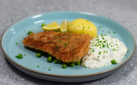 Panerad fisk med kokt potatis, ärtor och en krämig kall sås till fisk, garnerad med gräslök och citronklyftor.