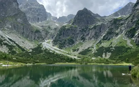 Piękne szlaki na Słowacji. Jezioro w górach odbija skaliste szczyty i zielone zbocza.