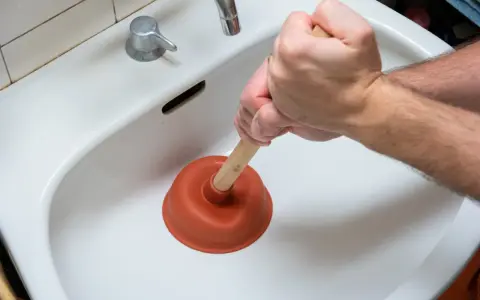 Main tenant utilise une ventouse pour déboucher un lavabo bouché.