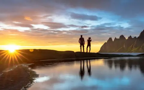 Två silhuetter står på en klippa vid havet och ser på solnedgången över Bodo, Norge. Bergskedja i bakgrunden.