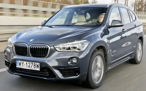 Ciemnoszary BMW X1 2025 z kierowcą za kierownicą, jadący po drodze.