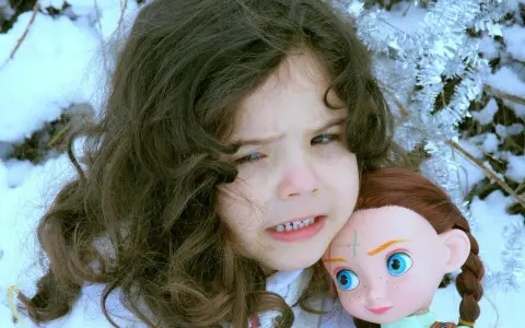 Ein Kind mit dunklen Haaren hält eine Puppe im Schnee. Das Kind sieht besorgt aus, als ob mein Kind Angst vor mir hätte.