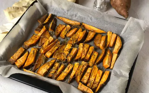 Patate dolci al forno tagliate a spicchi, condite con rosmarino e spezie, pronte per essere gustate.