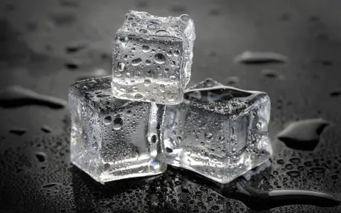 Drei eiswürfel mit Wassertropfen auf schwarzem Hintergrund. Die Frage, wie lange braucht Eis zum Gefrieren, wird hier visuell beantwortet.