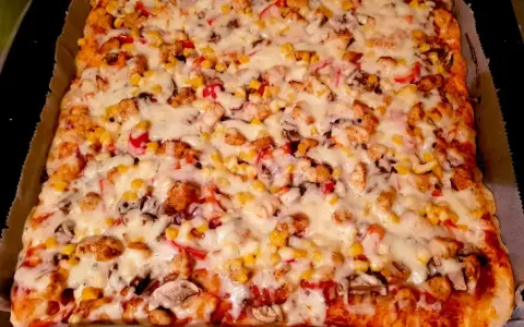 Pyszne, prostokątne ciasto na pizzę z suchych drożdży, obficie posypane kurczakiem, kukurydzą i serem.