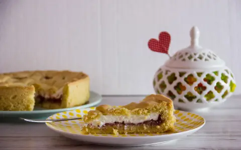 Slice of crostata with ricotta and jam on a yellow polka dot plate, with a whole crostata in the background.