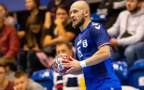 Mateusz Jachlewski, szczypiornista w niebieskiej koszulce z numerem 15, trzyma piłkę do piłki ręcznej.