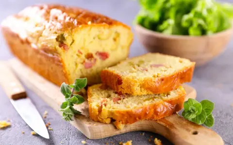 Tranche de cake jambon fromage dorée, garnie d'herbes fraîches, prête à être dégustée.