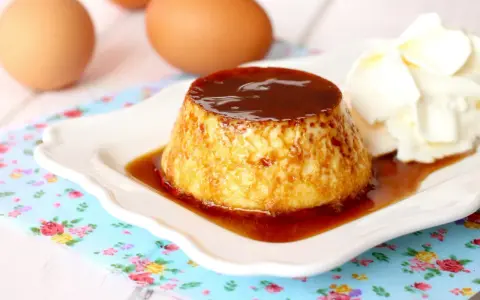 Delicioso flan de huevo casero con caramelo líquido y una porción de nata montada. Huevos frescos al fondo.