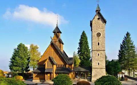 Drewniany kościółek i kamienna wieża z zegarem, jedne z głównych atrakcji Karpacz i okolice, na tle błękitnego nieba.