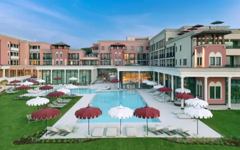 Un resort da sogno a Caorle, con piscina azzurra, lettini e ombrelloni rossi e bianchi. Un cavallino bianco potrebbe galoppare felice in questo paradiso.