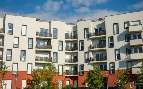 Immeuble moderne aux balcons noirs, un **idéal de la loge** avec ses façades blanches et sa base rouge. Ciel bleu et nuages.