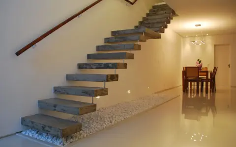 Escaleras rústicas modernas de hormigón flotante con pasamanos de madera. Un camino de guijarros blancos bordea la base.