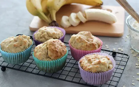 Fünf leckere bananenmuffins ohne zucker in bunten Förmchen auf einem Gitter. Bananen und Mehl im Hintergrund.
