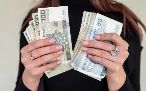 Dłonie z paznokciami w pastelowym różu trzymają pliki polskich banknotów 100 i 50 zł. To może być nagroda jubileuszowa.