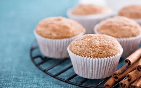 Leckere Apfelmus Muffins mit Zimt bestreut auf einem Gitter, daneben Zimtstangen.