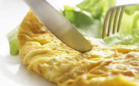 Un cuchillo corta una dorada tortilla francesa servida con hojas de lechuga fresca.