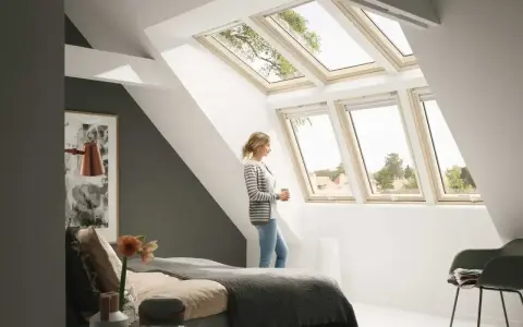 Kobieta w sypialni pod jasną, nowoczesną lukarną dachową, podziwia widok.