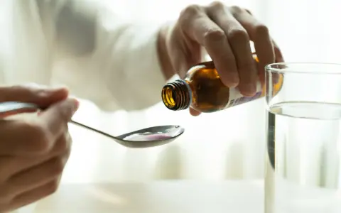 Dłoń wylewa płyn z butelki na łyżkę. To może być laktuloza w ciąży, pomocna przy problemach z wypróżnianiem.