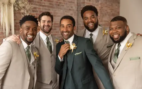 Groomsmen in light tan suits and one in a dark green suit, all smiling. They are dressed for a wedding, showing when grooms get suits.