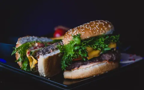 Dwa soczyste burgery z serem, sałatą i warzywami na ciemnym tle.