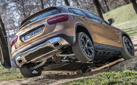 Złoty Mercedes GLA 220 4MATIC pokonuje nierówny teren, unosząc jedno koło.