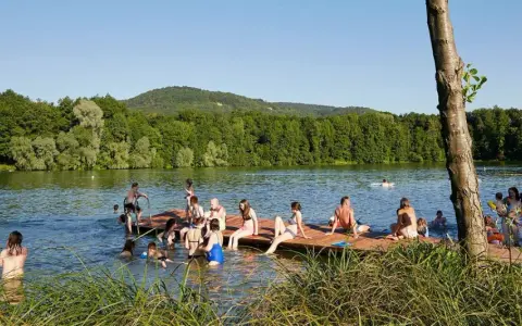 Menschen genießen einen sonnigen Tag am Baggersee Happurg. Sie sitzen auf einem Holzsteg, schwimmen und entspannen sich im Wasser.