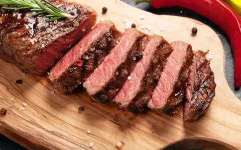 Perfekt stekt entrecote, skivad och serverad med rosmarin, pepparkorn och flingsalt på en träskärbräda. En röd chili ligger bredvid.