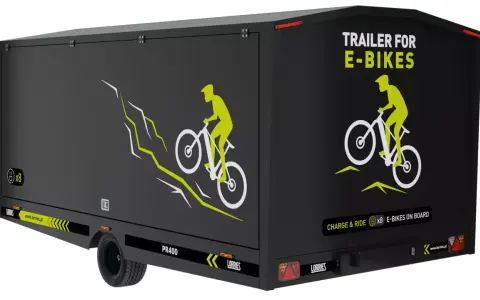 Czarna rowerowa przyczepa kempingowa z grafiką rowerzysty na górskim szlaku. Napis "TRAILER FOR E-BIKES" i "CHARGE & RIDE x8 E-BIKES ON BOARD".