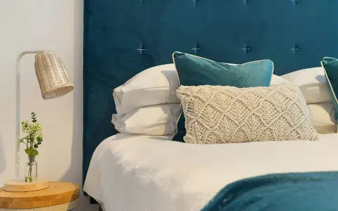 Cabecero de tela azul con cojines y lámpara de mimbre. Si buscas como limpiar cabecero de tela, este es un ejemplo de cómo mantenerlo impecable.