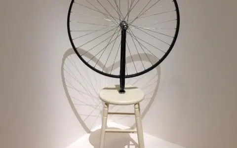 Roue de vélo fixée sur un tabouret, une œuvre emblématique de Marcel Duchamp, projetant une ombre fascinante.