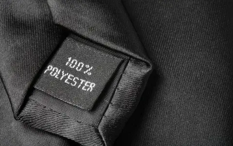Czarna metka z napisem "100% POLYESTER" na tle eleganckiego materiału. Czy poliester to dobry materiał?