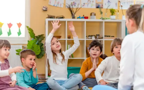 Niños atentos en clase, quizás buscando frases para profesores despedida. Una niña levanta la mano, ansiosa por participar.