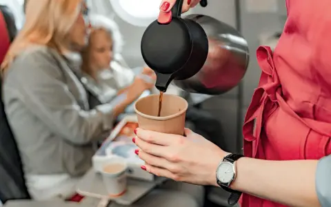 Na pokładzie samolotu stewardessa nalewa kawę do kubka. Pasażerowie zastanawiają się, czy można przewieźć kawę w samolocie, a odpowiedź brzmi: tak!