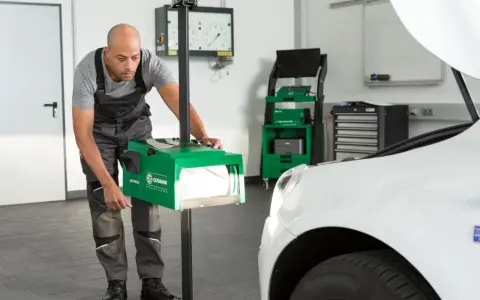 Mechanik dokonuje ręcznej regulacji świateł samochodu za pomocą zielonego urządzenia.