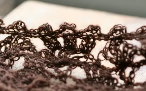 Close-up of a brown, lacy crocheted fabric with an openwork pattern.