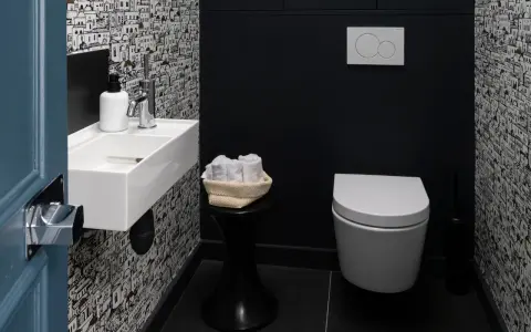 Une salle de bain moderne avec un papier peint original, un petit lavabo blanc, des serviettes roulées et une cuvette suspendue. La deco wc est soignée.