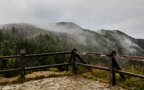 Mglisty poranek na Babiej Górze. Pasmo górskie otulone chmurami, widok z drewnianego tarasu.