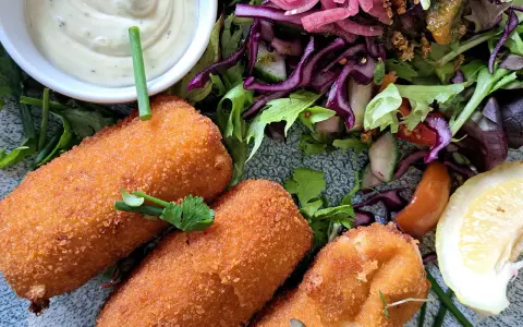 Croquetas doradas y crujientes con ensalada fresca, salsa y limón.