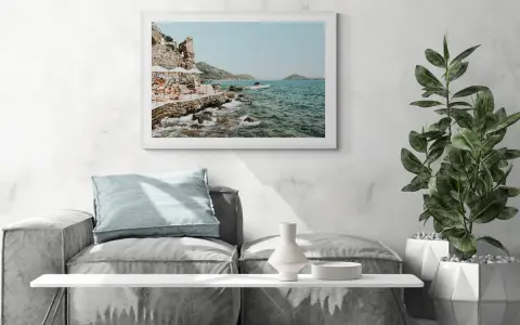 A framed print of a coastal scene, reminiscent of fine art photography galleries, hangs above a sofa. The artwork depicts a rocky shoreline with people relaxing under umbrellas.