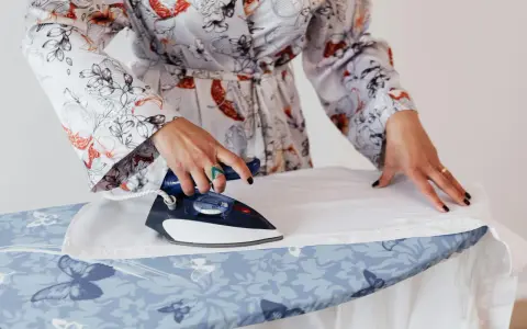 Mujer con bata estampada plancha lino blanco a mano sobre tabla con mariposas.