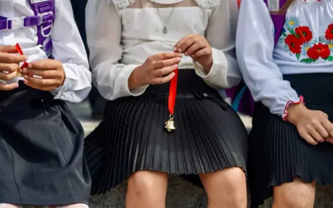 Trzy dziewczynki w szkolnych strojach, jedna trzyma dzwoneczek na wstążce. Czy w klasie 1-3 są świadectwa z paskiem?