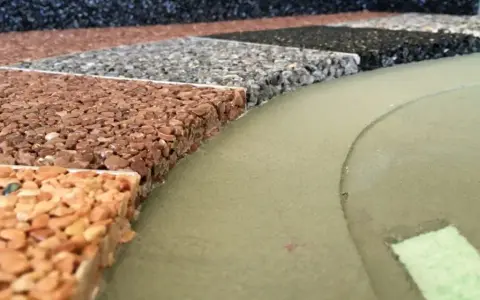 Przykładowe wykończenie tarasu betonowego: próbki nawierzchni z kamienia naturalnego w różnych kolorach, obok zielonej, gładkiej powierzchni.