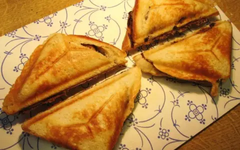Goldbraune Bananen-Toast-Sandwiches, dreieckig geschnitten, liegen auf einem Teller mit blau-weißem Muster.